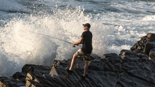 man fishing on wet rocks in splash zone